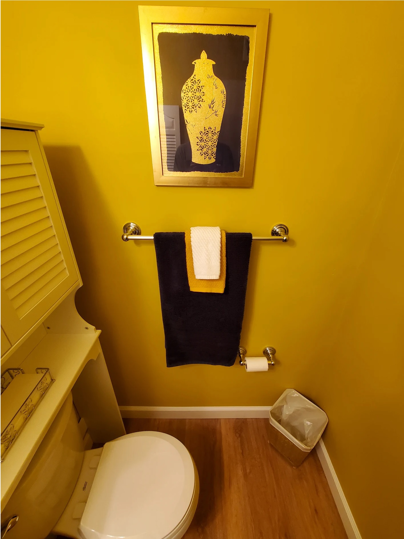 The same yellow half bath from the doorway, showing new towel bar, tissue holder, and wood-look flooring