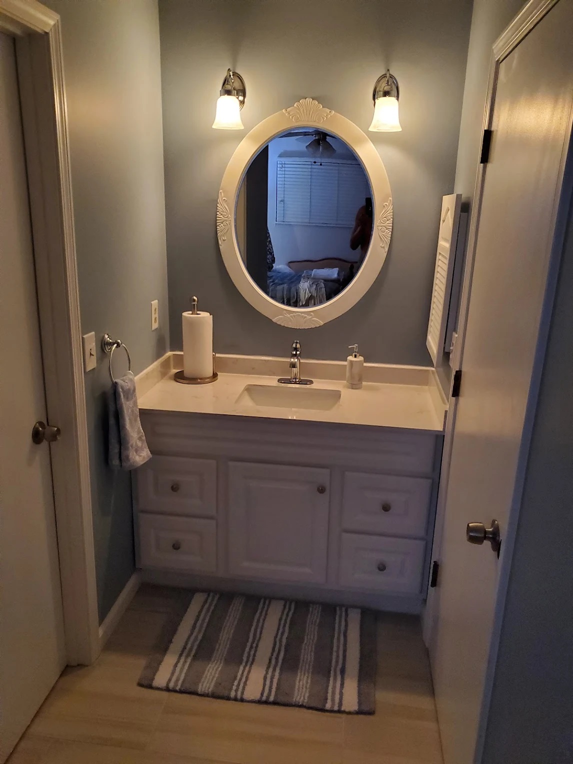 Powder room in soft sage with a white vanity, quartz top, oval mirror, and chrome sconces